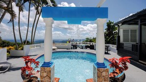 Une piscine bordée de pierres et de carreaux, un arc bleu et des plantes en pot.