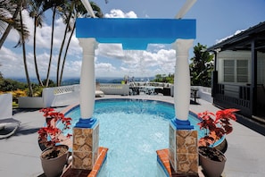 A swimming pool with a stone and tile border, a blue archway, and potted plants.