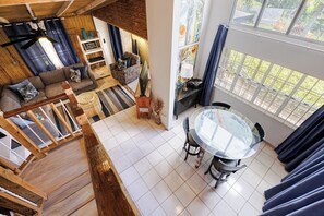 Een ruime woonkamer met een bank, een eettafel met stoelen, een trap en uitzicht door grote ramen.