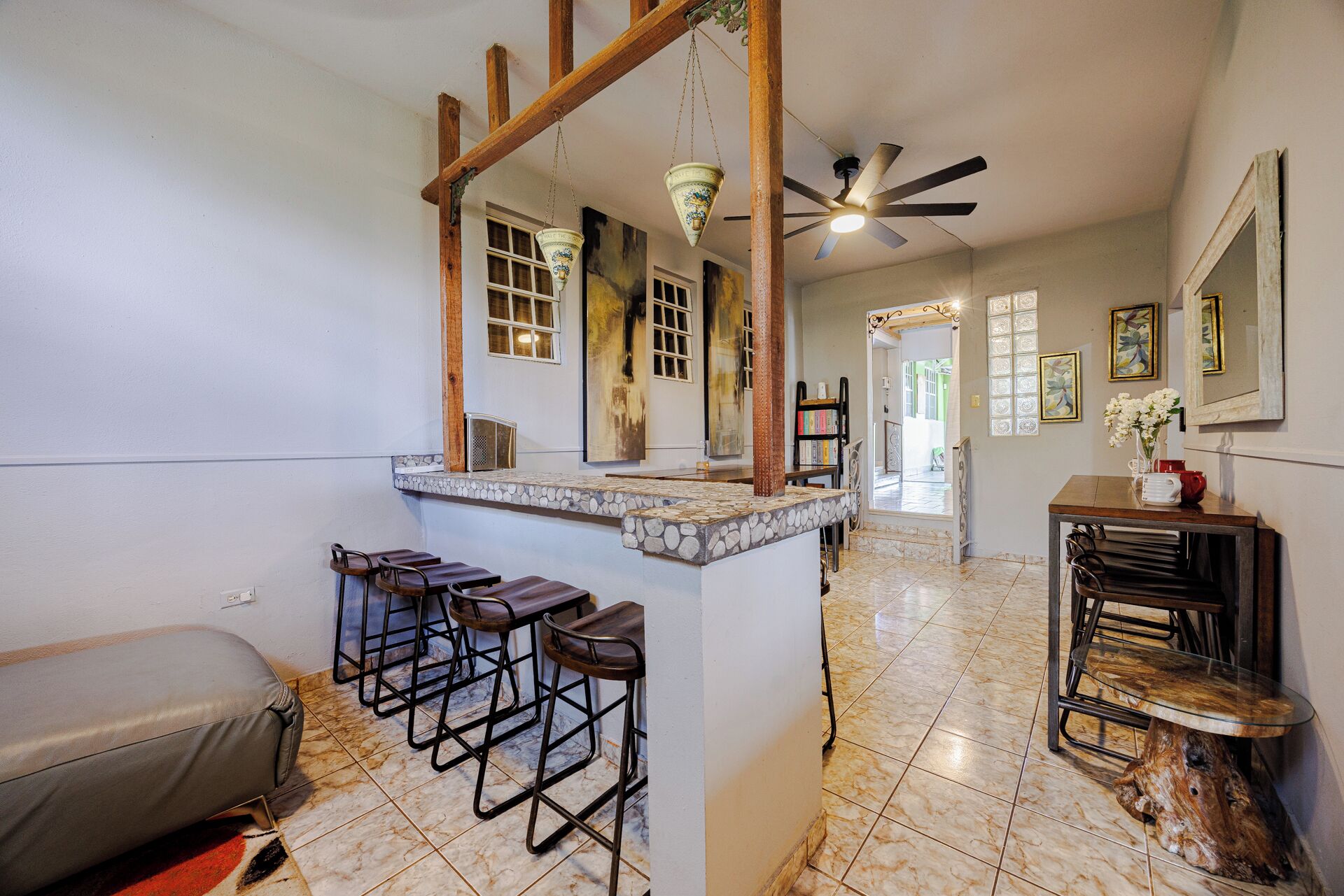 A bar area with stools, a ceiling fan, and a stone-tiled floor.
