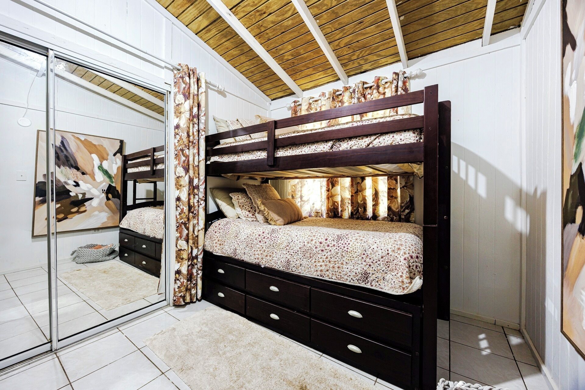 Uma cama beliche com estrutura de madeira, uma mesa de cabeceira com gavetas e um espelho grande.