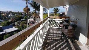 Un balcón con vista a una zona residencial, baranda de madera y una pequeña mesa con sillas.