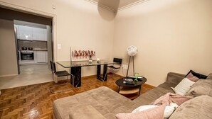 A modern living room with a sofa, a glass dining table, and a kitchen in the background. - Cozy Corner (Athens)