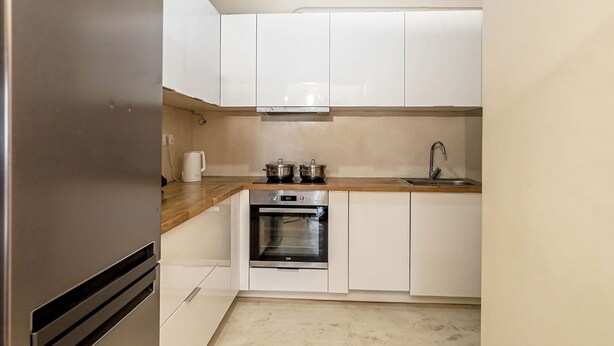 A modern kitchen with white cabinets, a stainless steel refrigerator, a built-in oven, and a wooden countertop. - Cozy Corner (Athens)