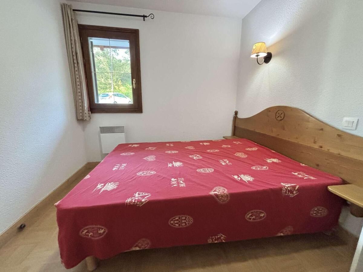 A small bedroom with a single bed, a window with curtains, a wall-mounted light, and a radiator.