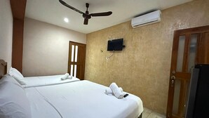 Une chambre d’hôtel avec deux lits, un ventilateur de plafond, un appareil de climatisation, une télévision et une porte en bois.