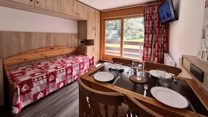 Una habitació acollidora amb un llit de fusta, una taula de menjador preparada per a dues persones i un televisor penjat a la paret.