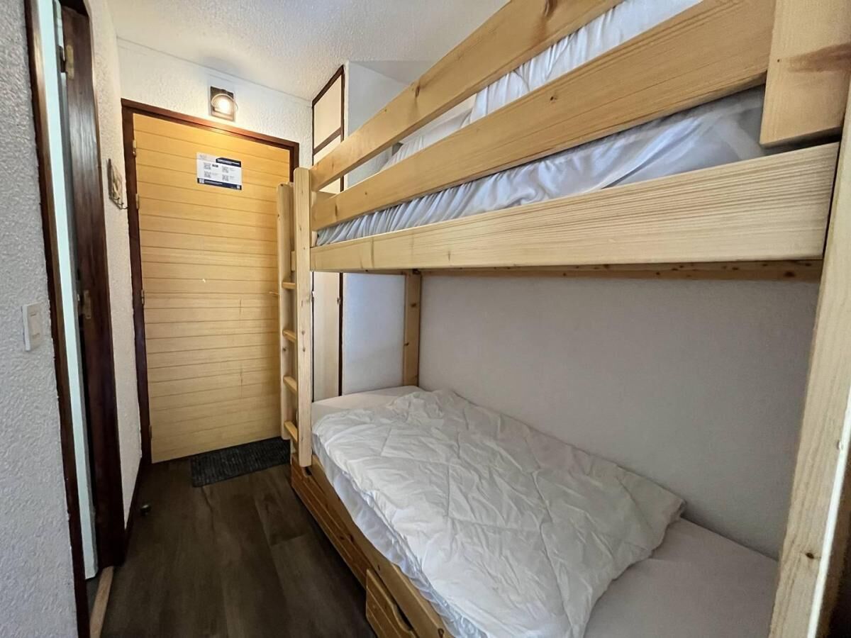 Une chambre avec un lit superposé, une porte en bois et une petite étagère.