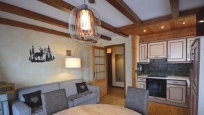 A cozy living room with a wooden ceiling, a dining table, and a kitchen area with white cabinets. - Wifi, 1st floor, balcony, parking, ski locker, 52m², Le Grand Bornand (Le Grand-Bornand)