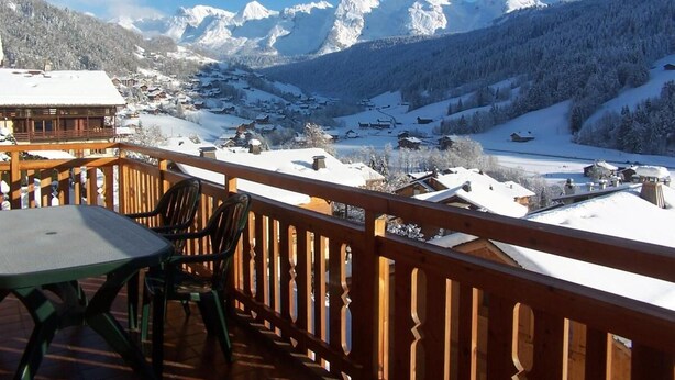 A wooden balcony with a table and chairs, overlooking a snow-covered village and mountains. - Wifi, 1st floor, balcony, parking, ski locker, 52m², Le Grand Bornand (Le Grand-Bornand)