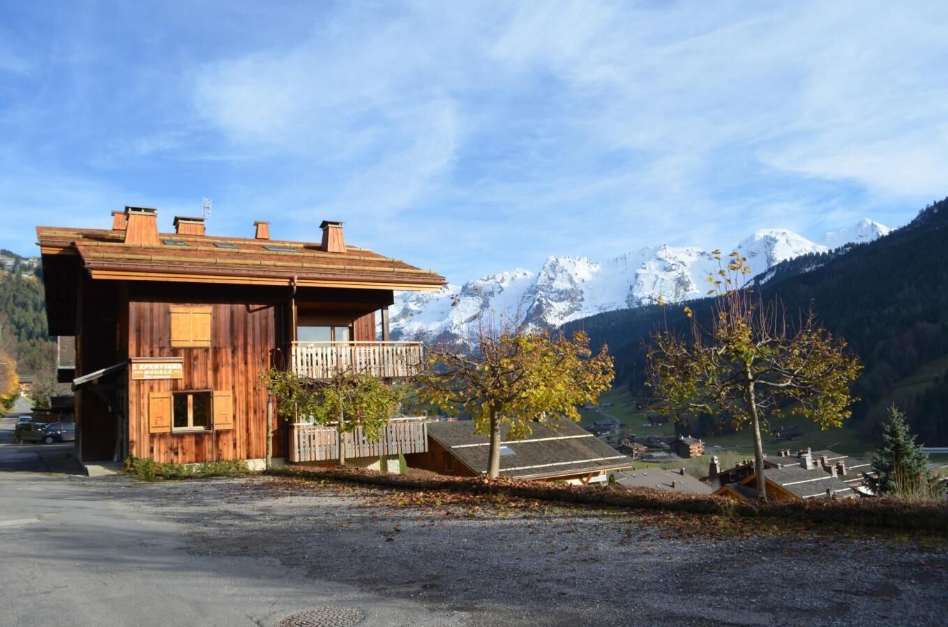 Een houten chalet met balkon, gelegen voor een achtergrond van besneeuwde bergen en een heldere lucht.