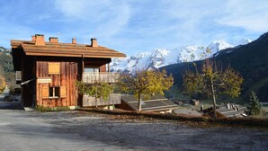 A wooden chalet with a balcony, set against a backdrop of snow-capped mountains and a clear sky. - Wifi, 1st floor, balcony, parking, ski locker, 52m², Le Grand Bornand (Le Grand-Bornand)