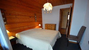 A cozy bedroom with a wooden ceiling, a bed with a white bedspread, a nightstand with a lamp, a dresser, and a chair. - Wifi, 1st floor, balcony, parking, ski locker, 52m², Le Grand Bornand (Le Grand-Bornand)
