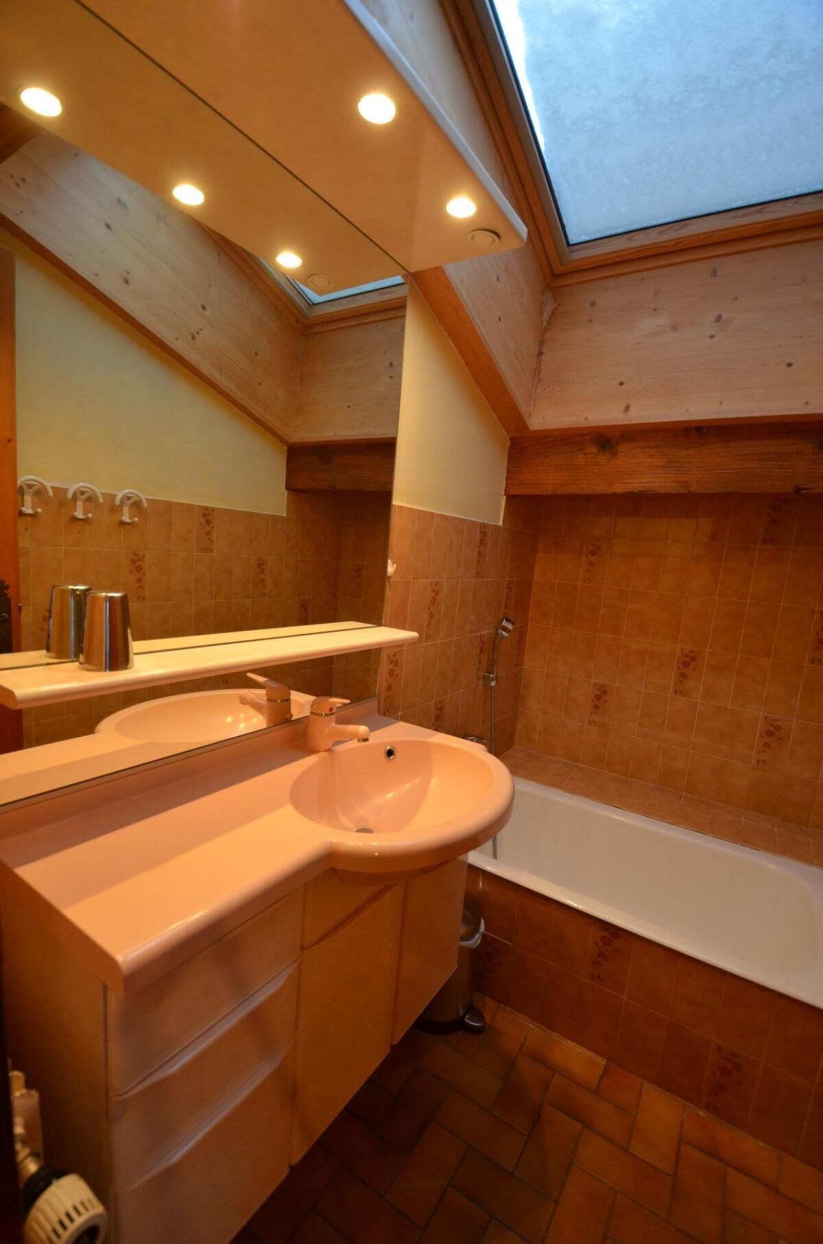 A bathroom with a skylight, wooden walls, a sink, and a bathtub.