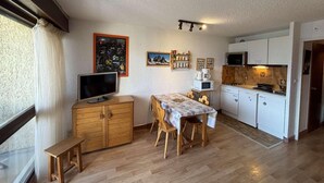 A compact living space with a dining area, kitchenette, and a television on a wooden cabinet.
