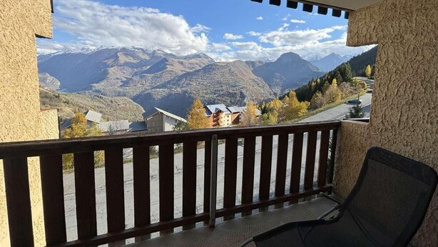 A balcony with a view of mountains, a chair, and a building in the background.