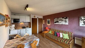 A compact living space with a kitchenette, a dining area, and a sofa with colorful cushions.