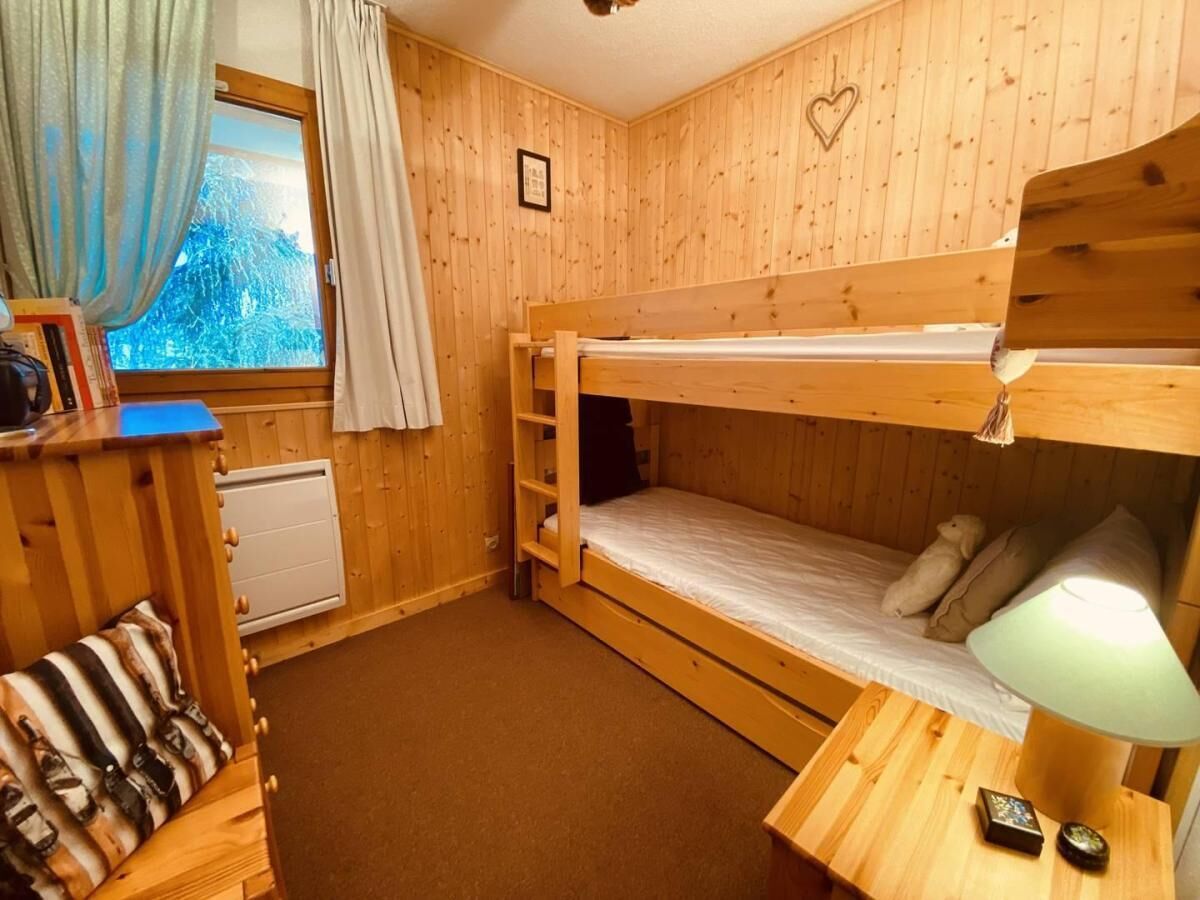 Une chambre avec un lit superposé en bois, un bureau, une lampe et une fenêtre avec des rideaux.