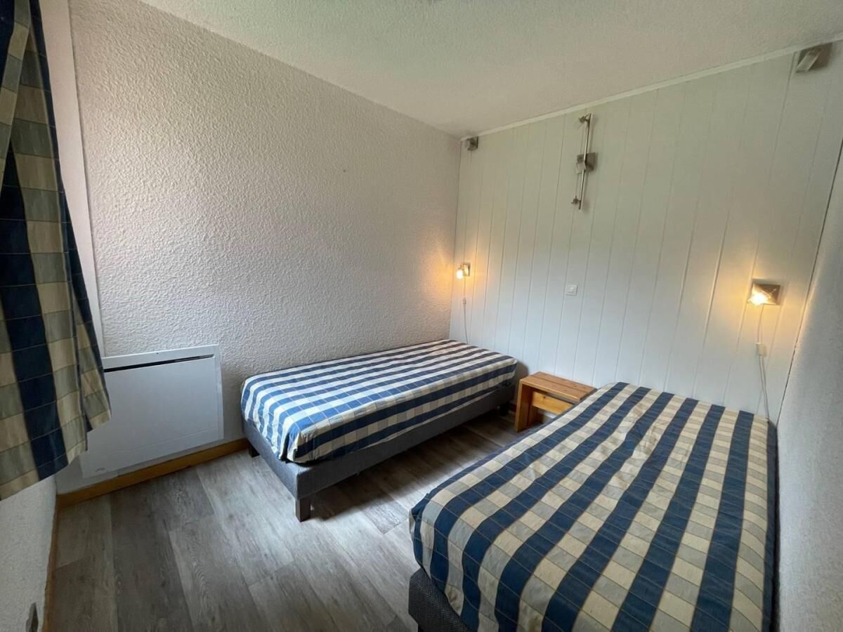 Een kleine, compacte kamer met twee eenpersoonsbedden, een houten nachtkastje en een wandradiator.
