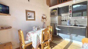 Uma área de refeições acolhedora, com uma mesa e cadeiras de madeira, uma cozinha com eletrodomésticos modernos e um ventilador de teto.