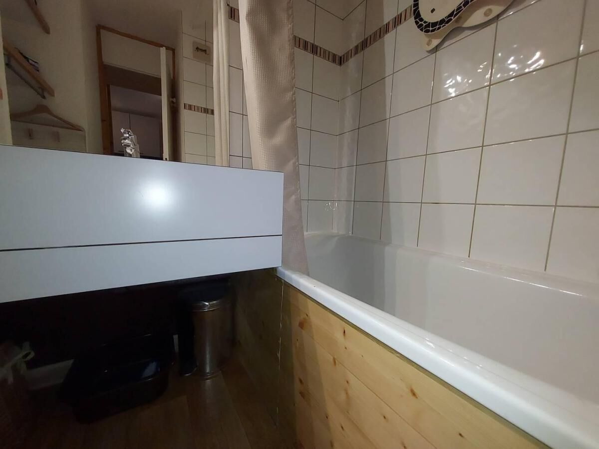 A bathroom with a white bathtub, wooden flooring, and a tiled wall.