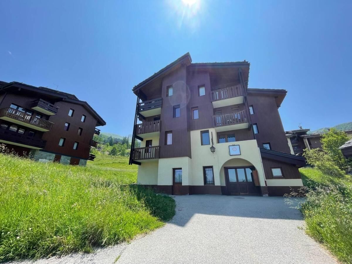 A multi-story building with balconies, a central entrance, and a gravel driveway.
