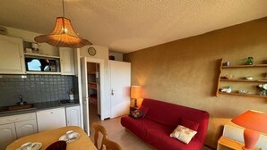 A compact living space with a dining area, a red sofa, a kitchen with a microwave, and a hanging light fixture. - 10m from ski slopes, view mountain, balcony, parking, ski locker, 23m², Auris en Oisans (Auris)
