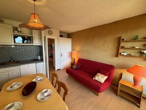 Ein kompakter Wohnbereich mit Essbereich, einem roten Sofa, einer Küche mit Mikrowelle und einer Pendelleuchte.