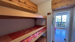 A bunk bed room with wooden headboards, a small window, and a door leading to a balcony. - 10m from ski slopes, view mountain, balcony, parking, ski locker, 23m², Auris en Oisans (Auris)
