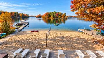 A lakeside beach with lounge chairs, kayaks, and a dock.
