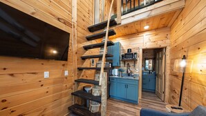 Ein Holzblockbau-Innenraum mit einer Treppe zu einem Schlafzimmer auf dem Dachboden, einer Küchenzeile und einer Sitzecke mit einem blauen Sofa.