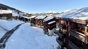 Un pueblo cubierto de nieve con edificios de madera, cielo despejado y montañas al fondo.