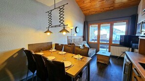 Un comedor con una mesa de madera dispuesta para seis personas, un sofá y un televisor al fondo.