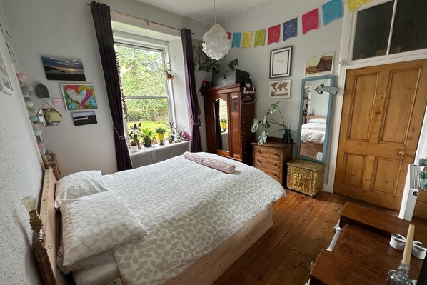 A bedroom with a bed, wooden dresser, and a window with curtains.