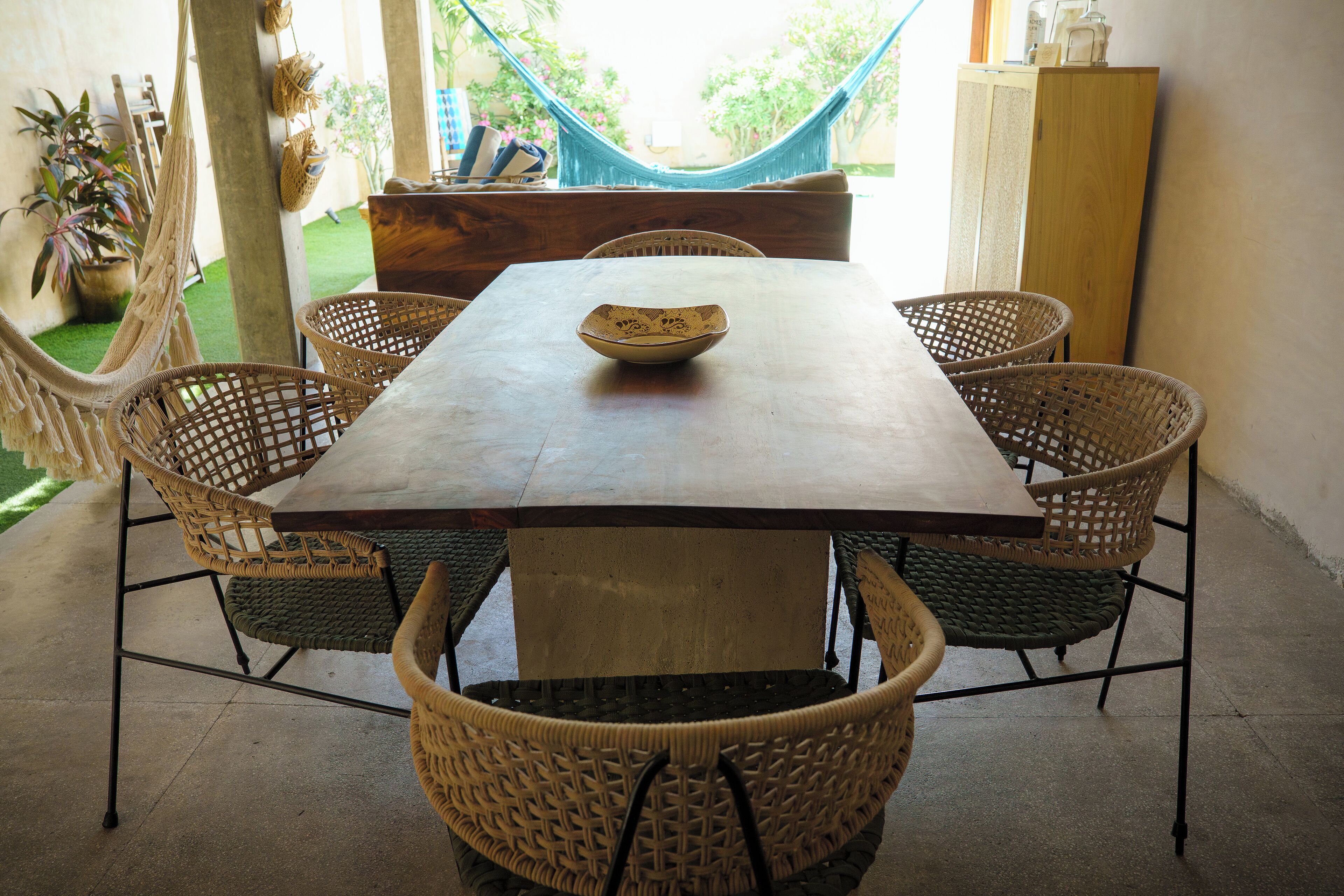 A dining area with a wooden table, wicker chairs, and a hammock in the background.