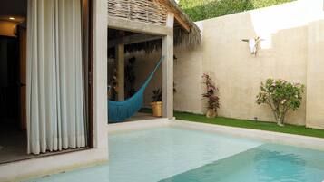 A pool area with a hammock, potted plants, and a thatched roof structure.