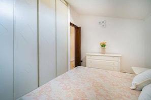 Ein Schlafzimmer mit Bett, Schminktisch, Nachttisch und einer Tür zu einem anderen Raum.