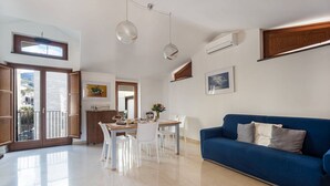 Un vaste espace de vie comprenant un canapé bleu, une table à manger avec des chaises, et une cuisine ouverte sur le reste de la pièce par une porte.
