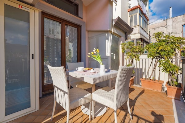 A balcony with a table and chairs, a potted plant, and a window with a curtain.