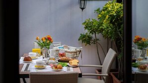 Une table à manger dressée avec des aliments pour le petit-déjeuner, des chaises en osier et une plante en pot.