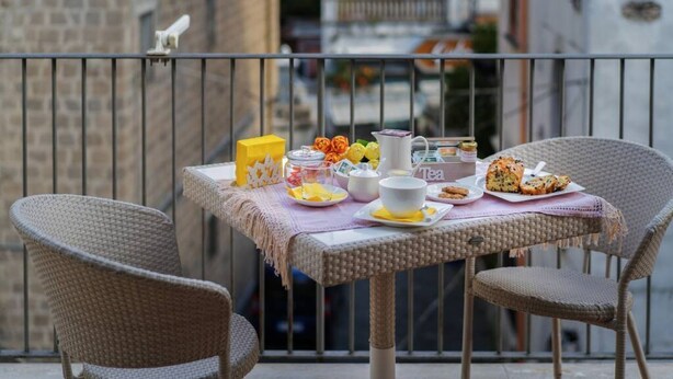 Un balcon avec des fauteuils en osier, une table dressée avec du thé, des pâtisseries et une boîte jaune.