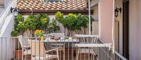A balcony with a table and chairs, a tiled roof, and potted plants.