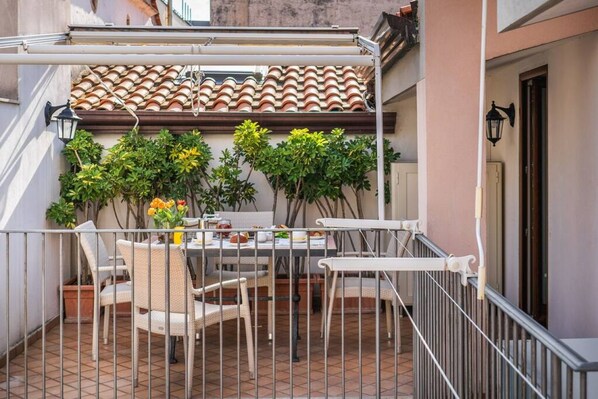 A balcony with a table and chairs, a tiled roof, and potted plants.