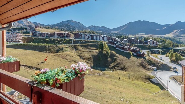 Un balcon offrant une vue sur un paysage montagneux, comprenant une station de ski et des immeubles résidentiels.