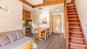 Une pièce chaleureuse avec un escalier en bois, un coin repas avec une table et des chaises, une cuisine avec des meubles en bois et un canapé à rayures.