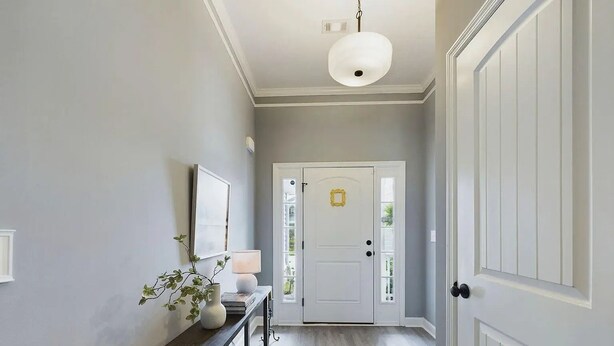 Ein Flur mit einer Bank, einem Blumentopf, einer Wandlampe und einer Tür mit goldfarbener Umrandung.