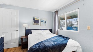 A bedroom with a bed, a nightstand, a lamp, and a window with a view of the outside. - Workforce Suites (Peru)