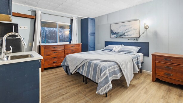 A bedroom with a bed, a dresser, a nightstand, a window with curtains, and a painting on the wall. - Workforce Suites (Peru)