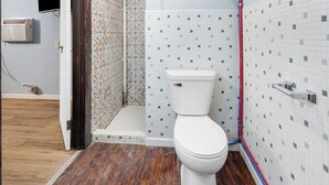 A bathroom with a white toilet, tiled walls, a shower area, and a wooden floor. - Workforce Suites (Peru)
