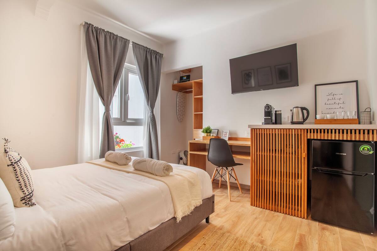 A modern bedroom with a bed, a desk, and a refrigerator.